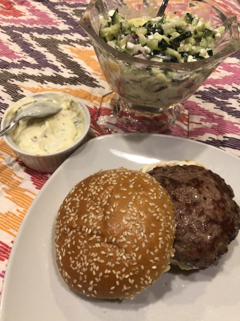 A lamb burger with bowls of lemon Oregano Aioli and Cucumber Feta Relish 