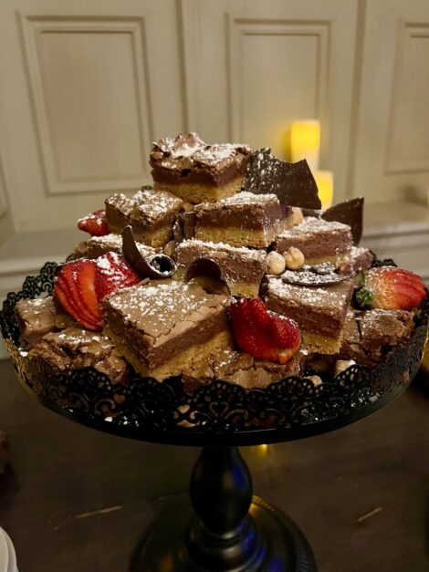 Nutella Gooey Butter Cake pieces piled on a plate and garnished with hazelnuts, fresh strawberries and chocolate shavings.