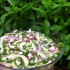 A bowl of cucumber salad sitting. in front of a bunch of mint.