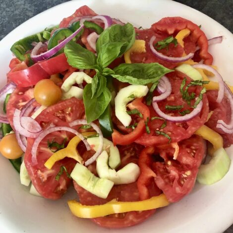 A platter of cut summer vegetables garnished with basil.