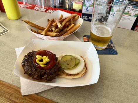 Hamburger with onion and pickles served at the bar with fries and a beer.