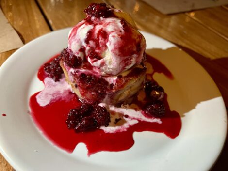 A plate of Spartina's warm bread pudding topped with melting vanilla ice cream and blackberry sauce.