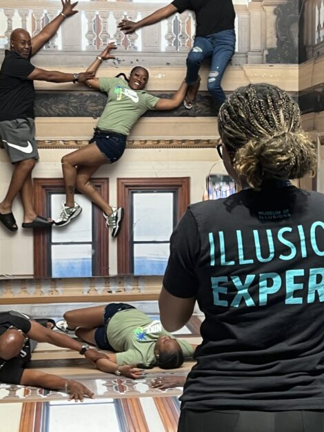 An illusion expert snapping a photo of a family fake falling off a balcony at the Museum of Illusions St. Louis.