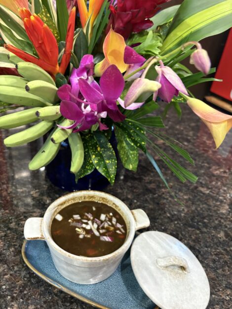 A bowl of Black Bean Soup sitting in front of a bouquet of tropical flowers.